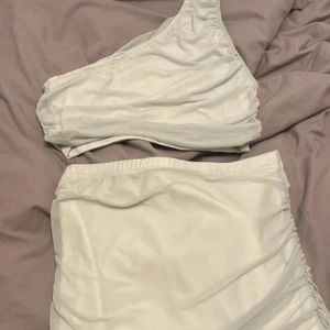 Ljusgrön set - Snyggt set med en axelbandstopp och hög midja kjol som går ner till fötterna. Toppen har en unik asymmetrisk design och underdelen är stilrent rynkad för en smickrande passform. Perfekt för sommarens stranddagar.