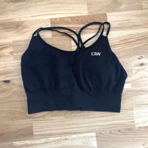 Sport-bh  - Svart ribbad sporttopp från ICIW med korsade axelband. Vadderade kupor som ger bra stöd. Helt oanvänd. 