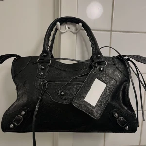 City bag - Valencia  - (OBS! inte begagnad! Finns även att beställa via vår hemsida www.ivysthlm.se) CITY BAG – Den perfekta statment väskan som livar upp varje vardags-outfit. Lika praktisk som snygg och fungerar både till skola & fest – Ja, din dator får plats! (väskan levereras med ett långt, justerbart axelband för extra bekvämlighet) Storlek: 38×10×23 cm Finns även tillgänglig i grå och röd! Äkta läder 