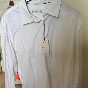 Vit skjorta från MNG - Säljer en stilren vit skjorta från MNG i slim fit. Skjortan har långa ärmar och klassisk krage, perfekt för en elegant look. Den är tillverkad i ett lätt och bekvämt material.