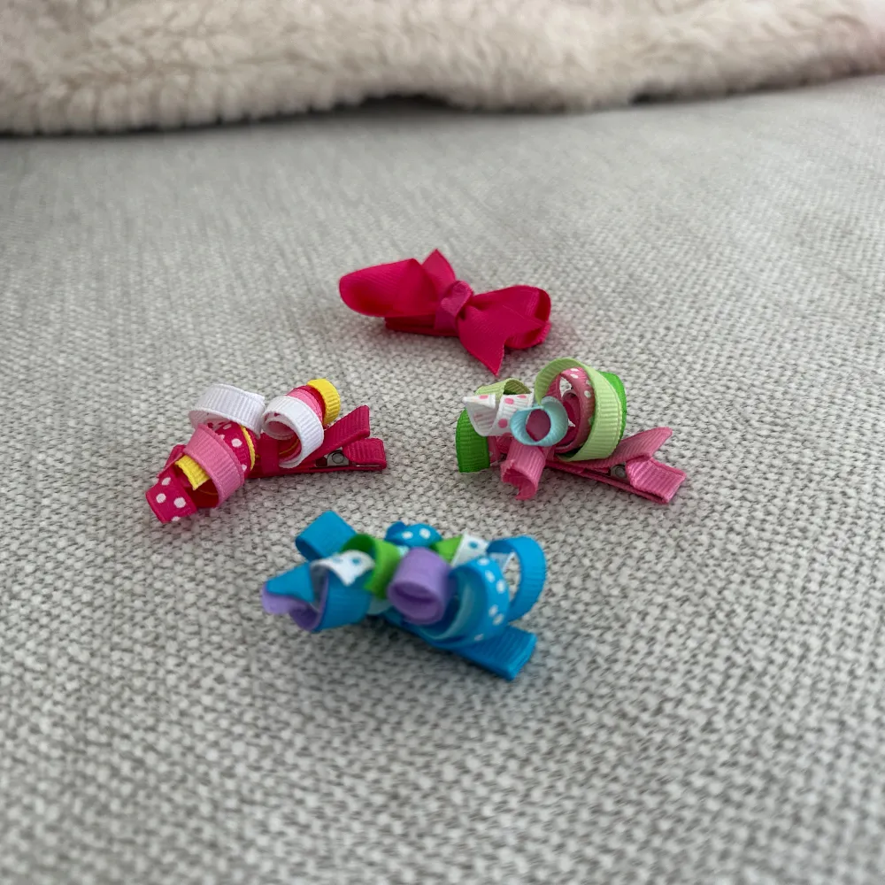 Säljer ett set med fyra färgglada hårspänne dekorerade med rosetter. hårspänne har olika färger och mönster, inklusive prickiga och randiga detaljer. Perfekta för att liva upp vilken frisyr som helst!. Asusteet.