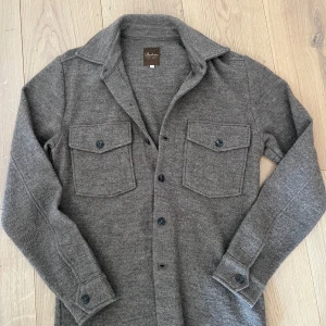 Brun stickad kashmir overshirt med fickor - Säljer en stilren brun overshirt från Stenströms Den har långa ärmar och två praktiska bröstfickor med knappar. Perfekt för lager-på-lager-stil under kyligare dagar. Knapparna framtill ger en klassisk look. Den är använd 0 gånger, och priset kan diskuteras 