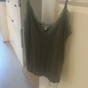 Grön linne från Amisu - Säljer ett grönt linne från Amisu med spetsdetaljer längs kanterna. Linnet har en v-ringad design och tunna axelband. Perfekt för varma dagar eller som ett lager under en tröja.