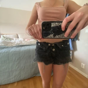 Svarta jeansshorts med fransar - Säljer ett par svarta jeansshorts med fransiga kanter och slitna detaljer. Shortsen har en knappgylf.