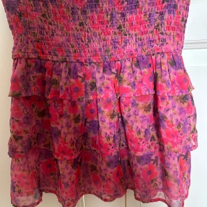 Blommig kjol med volanger - Söt blommig kjol i rosa med volanger. Perfekt för sommarens. Den har en smockad överdel som ger en bekväm passform. Ser ut som ny!