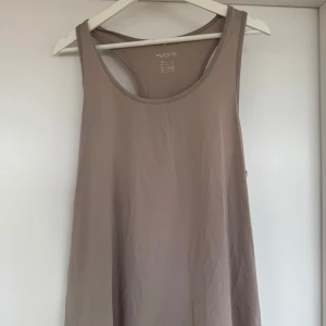 Beige träningslinne från H&M Move - Säljer ett beiget träningslinne från H&M Move. Toppen har en enkel design med rund halsringning och ärmlös stil, perfekt för träning eller en avslappnad dag. Materialet är mjukt och bekvämt.