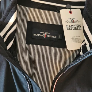 Marinblå bomberjacka från Hampton Republic - Snygg svart bomberjacka från Hampton Republic med randigt foder och dragkedja framtill. Jackan har ribbade muddar vid ärmslut och nederkant samt 2 praktiska innerficka med dragkedja. Perfekt för en stilren look.