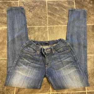 Blå jeans från Levi's - Säljer ett par klassiska blå jeans från Levi's med elastisk midja och snörning. De har en traditionell femficksdesign och en snygg tvättad look. Perfekta för en avslappnad stil.