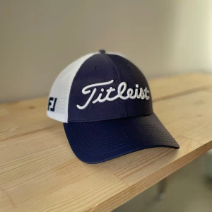 Titleist Keps - Snygg keps från Titleist i mörkblått och vitt med broderad logga framtill. Kepsen har en justerbar baksida i mesh för bra ventilation och komfort. Perfekt för golfbanan eller en solig dag ute.