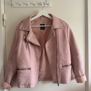 Rosa quiltad jacka från Atmosphere - Snygg rosa skinnjacka från Atmosphere med quiltad design och dragkedjor i size 38. Jackan har långa ärmar och en cool bikerstil med detaljer som knappar och dragkedjor på fickorna. Perfekt för våren🌸