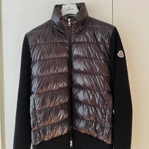 Moncler Cardigan Tricot - Snygg svart cardigan från Moncler🤩. Den har stickade ärmar och rygg samt en hög krage för extra värme. Håller värme även i minusgrader❄️ Mycket bra skick och inga defekter. Använd max 3 gånger, säljer pga använder knappt. Nypris 10800