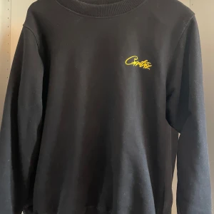 Svart sweatshirt med gul broderad text - Svart sweatshirt från Corteiz med gul broderad logga på bröstet. Riktigt snygg tröja men tyvärr för liten för mig. Nypris 800kr endast använd några gånger.