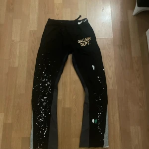 Svarta byxor från Gallery Dept. - Snygga svarta byxor från Gallery Dept. med unika färgstänk och tryck. Byxorna har en elastisk midja för extra komfort och är tillverkade i bomull. Perfekta för en avslappnad stil med en konstnärlig touch.