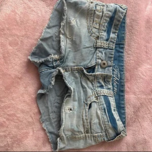 Ljusblå jeansshorts från Fishbone - Säljer ett par ljusblå jeansshorts från Fishbone med slitna detaljer och fransar. Shortsen har en knapp och dragkedja framtill samt fickor både fram och bak! Jättesnygga!!