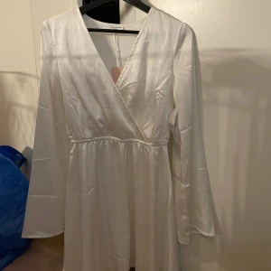 Vit studentklänning - Säljer en elegant vit omlottklänning från Bubbelrom. Klänningen har långa ärmar och en v-ringad design som ger en stilren look. Perfekt för speciella tillfällen eller en fin middag. 💫Den är i nytt skick pris lappen finns kvar