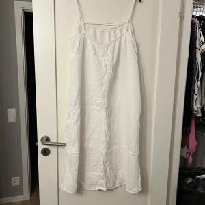 Vit klänning från H&M - Säljer en enkel och stilren vit klänning från H&M. Klänningen har smala axelband och en luftig passform, perfekt för varma dagar. Tillverkad i ett lätt och bekvämt material.