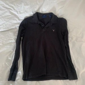 Svart långärmad pikétröja från Gant - Säljer en stilren svart långärmad pikétröja från Gant. Tröjan har en klassisk krage och knappar framtill. Perfekt för en avslappnad men ändå snygg look. 🖤