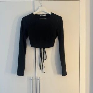 Svart croppad topp - Snygg svart topp med långa ärmar och öppen rygg. Toppen är croppad och har knytband i ryggen för en stilren look. Perfekt för fest!! Storlek:S🩷🫶🏼