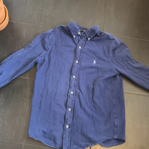 Blå skjorta från Ralph Lauren - Snygg blå skjorta från Ralph Lauren med klassisk krage och knappar framtill. Skjortan har långa ärmar och en broderad logotyp på bröstet. Perfekt för en stilren look.