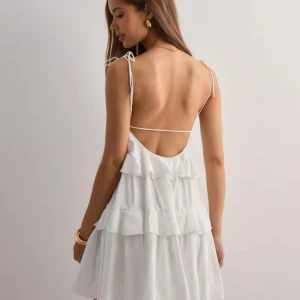 Vit volangklänning med öppen rygg från Nelly - Säljer min superfina vit kortklänning med volanger och tunna axelband som knyts på axlarna. Klänningen har öppen rygg med smal rem och är tillverkad i ett lätt, flowy material. Aldrig använd och prislappen är kvar!