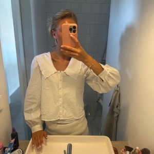 Vit skjorta med stor krage - Vit skjorta i bomull med oversized, vågig krage och knappar framtill. Skjortan har långa puffärmar med breda manschetter och en rak, något croppad passform. Perfekt för dig som gillar trendiga detaljer och en clean look.
