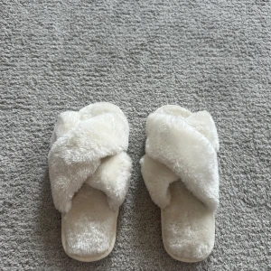Vita fluffiga tofflor  - Supermjuka och mysiga tofflor med korsade band över foten. Platt sula och öppen tå, i storlek 38-39. Aldrig använda! 