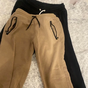 2-pack mjukisbyxor från Warp och svart par - Två par mjukisbyxor, ett par i beige från Warp med svarta dragkedjor på fickorna, snörning i midjan och tryck på benet. Det andra paret är helsvart med vit snörning i midjan. Båda är i mjukt bomullsmaterial och har avslappnad passform. Tillsammans kostar de 80 kr. Man kan absolut köpa de separata också för 45 kr styck