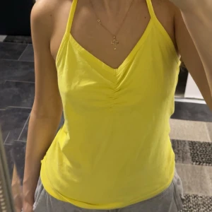 Gul linnetopp från Marwin - Snygg gul linnetopp från Marwin med smala axelband och v-ringning. Toppen har rynkade detaljer framtill och är tillverkad i mjuk bomull, perfekt för varma dagar. Enkel och fräsch design som ger en somrig vibe, passar även s.