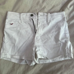 Vita jeansshorts från Hollister - Snygga vita jeansshorts från Hollister med klassisk femficksdesign och uppvikta benslut. Shortsen har låg midja, bälteshällor och dragkedja framtill. Perfekta för varma dagar och ger en fräsch look till sommargarderoben.