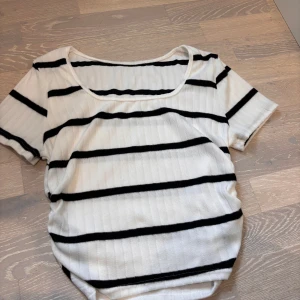 Randig ribbad topp i vitt och svart - Snygg ribbad topp med svarta horisontella ränder på vit botten. Modellen har korta ärmar och rund halsringning, perfekt för en chill och stilren look. Passar till både jeans och kjol för en enkel men trendig outfit.