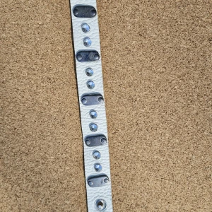 Vitt läderarmband med nitar och stenar - Coolt vitt armband i läder med silvriga nitar och blanka stenar som ger extra bling. Armbandet har tryckknappsstängning och detaljer i metall för en edgy look. Perfekt accessoar för att lyfta din outfit med lite rockig känsla.