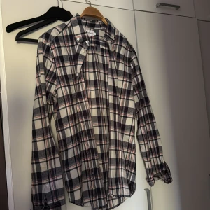 Rutig skjorta från East West - Snygg rutig skjorta från East West i svart, vit och röd. Skjortan har klassisk krage, knäppning framtill och långa ärmar. Perfekt för en avslappnad och cool stil. Tillverkad i mjuk bomull som känns skön mot huden.