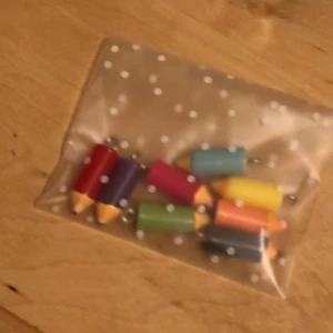 Ett pack med Färgglada pennhängen till smycken - Säljer ett set med 8 st små berlocker formade som färgglada pennor. Perfekta att använda till halsband, armband eller örhängen. Hängena kommer i rött, lila, grönt, blått, gult, orange, rosa och svart. De är tillverkade i plast och har en metallögla för enkel montering.