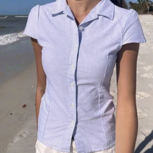 🌸Sommrig Ljusblå- och vitrandig skjorta 🌸 - Snygg kortärmad skjorta med smal passform och klassisk krage. Skjortan har ljusblå och vita ränder, knäppning framtill och är tillverkad i ett lätt bomullstyg. Perfekt för varma dagar när du vill ha en fräsch och stilren look.🌼🌻 Somrig och stjäl all uppmärksamhet!💐💐 priset kan diskuteras♡