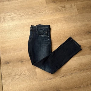 Replay mörkblå jeans straight fit - Säljer ett par mörkblå jeans från Replay med klassisk femficksdesign och snygga slitningar framtill. Jeansen har raka ben och normal passform, med Replay-logga på bakfickan. Perfekta för dig som gillar en stilren och tidlös look. Storlek 34-32