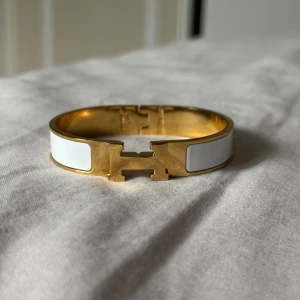 H armband - Snyggt H  armband i guldpläterad metall med vita emaljdetaljer. Armbandet har den ikoniska H-formade låset framtill. Pris kan diskuteras vid snabb affär.