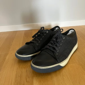 Svarta Lanvins  - Snygga svarta sneakers med crocomönstrad sida och tå i slätt skinn. Skorna har snörning och vit sula med mörkblå kant. Perfekta för dig som gillar stilrena detaljer och vill sticka ut lite extra. Inget OG följs med.
