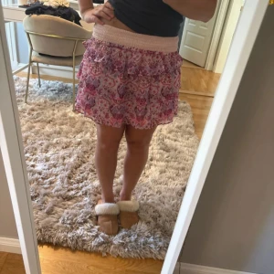 Rosa volangkjol med mönster - Supersöt kort volangkjol i rosa och lila toner med blommigt mönster. Kjolen har bred smock i midjan och flera lager volanger som ger en flowy känsla. Perfekt för sommarens alla tillfällen och lätt att matcha med en enkel topp. Den är i barnstorlek 152-164 men sitter snyggt på mig som är 161cm lång!