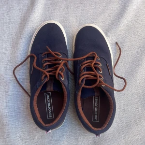 Mörkblå sneakers från Jack & Jones - Snygga mörkblå sneakers från Jack & Jones med bruna snören och detaljer. Ovandel i textil och vit platt sula. Perfekta för en avslappnad och stilren look. Klassisk rund tå och diskret logga på sidan.