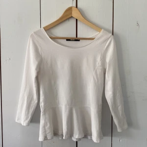 Vit peplumtop från Bik Bok - Säljer en vit topp från Bik Bok med rund halsringning och trekvarts ärmar. Toppen har en markerad midja och volang nertill som ger en snygg siluett. Perfekt att styla med jeans eller kjol för en söt och fräsch look.