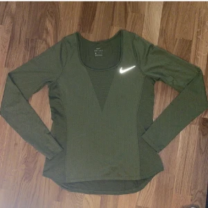 Grön långärmad träningströja Nike - Snygg grön långärmad träningströja från Nike med reflekterande logga på bröstet. Tillverkad i lätt och ventilerande material som passar perfekt för löpning eller gym. Smickrande passform och rundad halsringning.