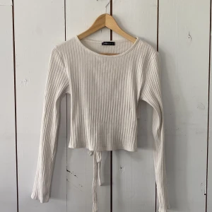 Vit ribbad omlottopp från FB Sister - Vit långärmad ribbad topp från FB Sister med croppad passform och snygg omlottdetalj med knyt i ryggen. Toppen har rund halsringning och är tillverkad i ett mjukt, stretchigt material som sitter skönt på kroppen. Perfekt för dig som gillar trendiga och stilrena plagg. Toppen är skrynklig eftersom den är nytvättad.💕