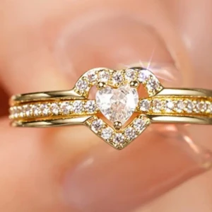 Guldring med hjärtformad sten storlek 7 - Superfin guldfärgad ring med gnistrande stenar och en hjärtformad klar sten i mitten. Ringen har dubbla band med små glittrande stenar längs hela ovansidan och ett hjärta som verkligen poppar. Perfekt för dig som älskar bling och romantiska detaljer.