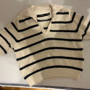 Randig stickad tröja från Vero Moda - Superfin stickad tröja från Vero Moda i beige med marinblå ränder. Tröjan har v-ringning, krage och korta ärmar. Perfekt till jeans för en chill och trendig look. Materialet är mjukt och skönt, och passformen är normal. Nypris 349 kr och aldrig använt.