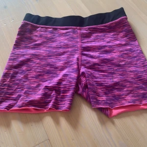 Rosa sportshorts från H&M - Snygga sportshorts från H&M i rosa och lila med svart midjeresår. De har ett coolt mönster och är gjorda i stretchigt syntetmaterial. Har klippt av dessa eftersom det var ett par träningsbyxor innan. Säljer dom för har för många liknande!❤️