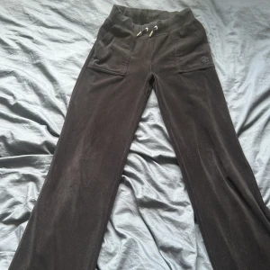 Svarta mjukisbyxor från Juicy Couture - Svarta mjukisbyxor från Juicy Couture i mjuk velour med bred resår och snörning i midjan. Byxorna har raka ben, stora fickor fram och bakficka med tryckknappar och JC-logga. Perfekta för chill eller streetstyle. Storlek xxs men har töjts ut så jag med storlek S kan ha de.