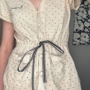 Prickig sör babydoll topp - Söt prickig babydoll topp med rosetter på fickorna, den har ett band runt midjan för en finare passform! Jag är xs men passar mig fint även om det är M! 