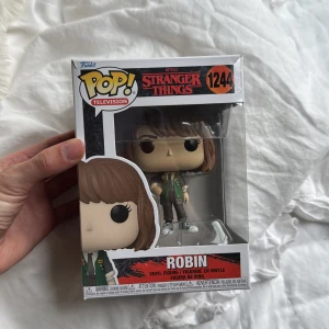 Stranger Things: Robin (Funko Pop! #1244) - Cool Funko Pop! vinylfigur av Robin från Netflix-serien Stranger Things. Perfekt för fans och samlare som vill ha en unik detalj till sitt rum eller hylla. Figuren är ny i originalförpackning och passar dig som älskar popkultur och spännande berättelser. Pris kan diskuteras! 