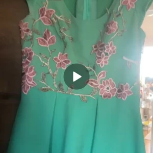 Turkos klänning med blommig brodyr - Superfin turkos klänning med broderade rosa blommor över bröstet och axlarna. Klänningen har en rund halsringning och är ärmlös, med en lätt utställd kjol. Perfekt för dig som vill sticka ut med färg och detaljer!