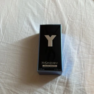 Yves Saint Laurent Y EdT 100ml - Yves Saint Laurent Y Eau de Toilette 100ml. Snygg, stilren flaska i transparent glas med svart kork och silverdetaljer. Doften är fräsch och maskulin, perfekt för dig som gillar moderna och eleganta parfymer. Kommer i originalförpackning med blå och svart design.